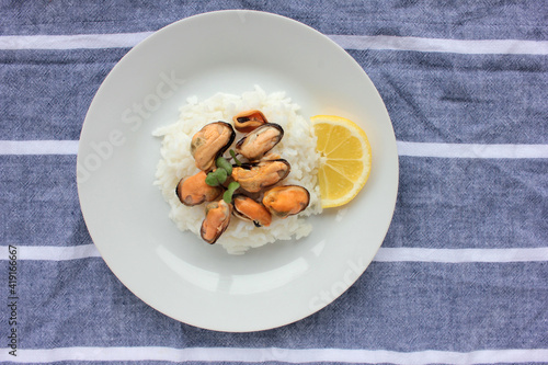 Mussel risotto on white plate on table. Top view of white rice with seafood and lemon slice on striped cloth napkin background. Copy space. Healthy eating concept 