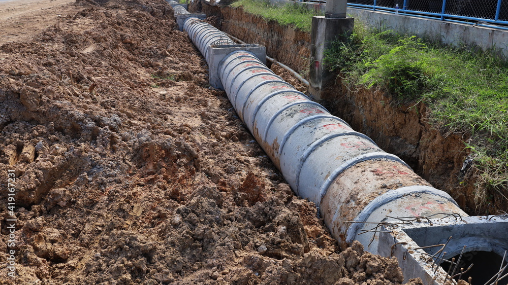 Row the concrete drain in the hole. Sewerage in the construction area beside the highway. Urban drainage infrastructure with copy area. Selective focus Row the concrete drain in the hole. Sewerage in the construction area beside the highway. Urban drainage infrastructure with copy area. Selective focus