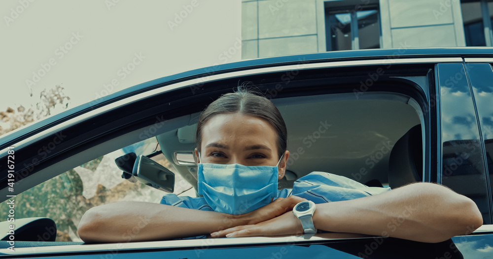 young woman in medical mask sitting on driver seat and looking at camera from open window young woman in medical mask sitting on driver seat and looking at camera from open window