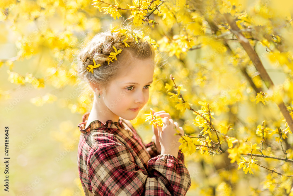 Fototapeta premium girl sniffs yellow flowers. A child on the background of forsythia. Spring portrait of a child with flowers in her hair