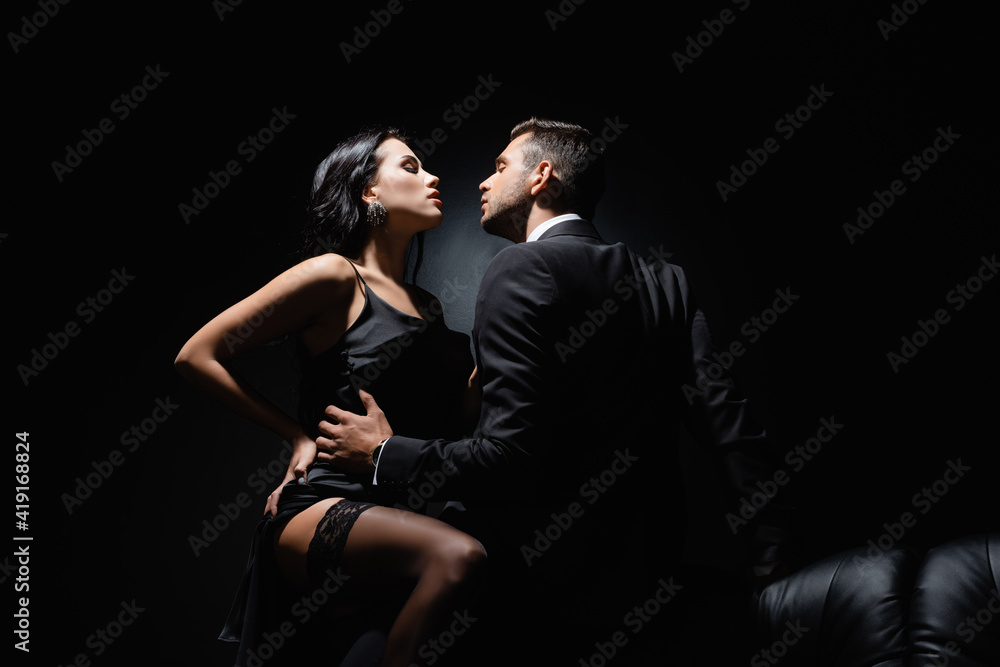 Man in suit touching passionate woman in dress on black background with smoke