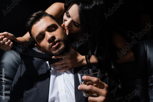 Sexy woman biting ear of boyfriend with whiskey isolated on black