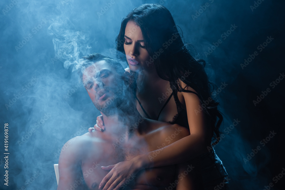 Brunette woman touching sexy man on black background with smoke Brunette woman touching sexy man on black background with smoke