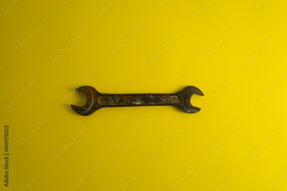 The old rusty wrench on the yellow background with traces of dirt The old rusty wrench on the yellow background with traces of dirt