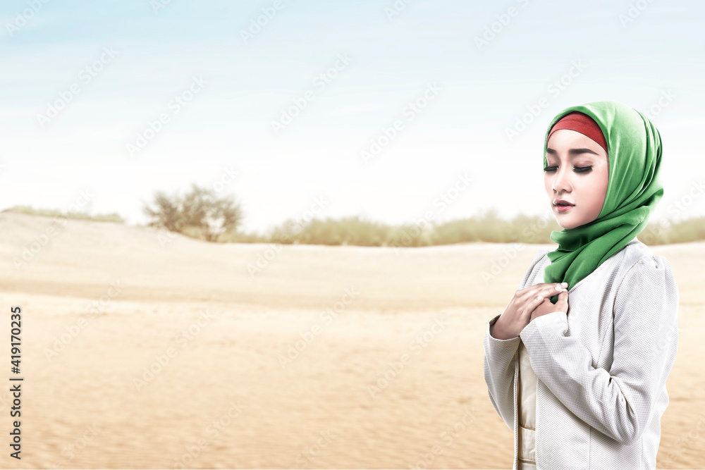 Asian Muslim woman in a veil standing while raised hands and praying Asian Muslim woman in a veil standing while raised hands and praying