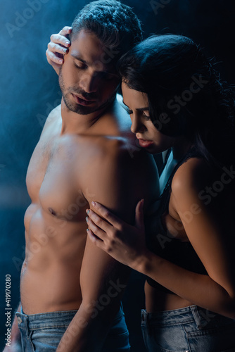 Sexy woman hugging shirtless man in jeans on black background with smoke