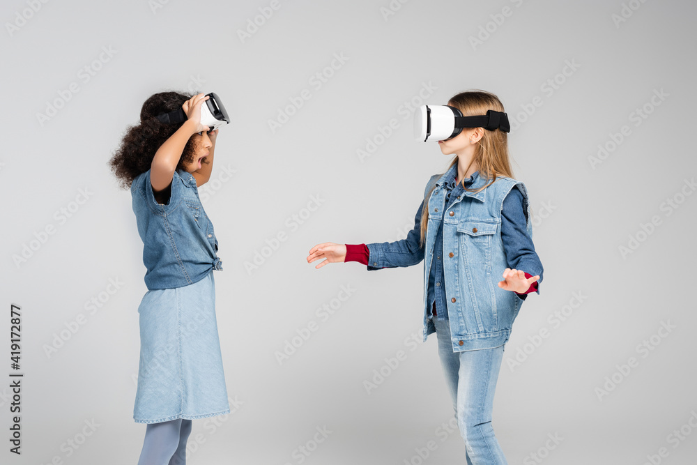 amazed african american girl looking at friend gaming in vr headset on grey amazed african american girl looking at friend gaming in vr headset on grey