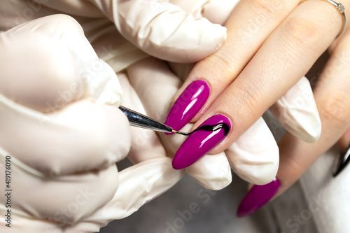 Nail design of a young girl is drawn by a manicure master with a thin brush in a beauty salon. Close-up