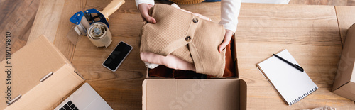 partial view of showroom owner packing clothes into box, banner photo