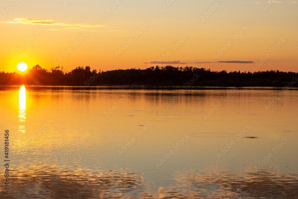 A colorful sunny sunset is reflected on the surface of the calm lake.
