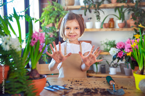 Little girl gardener plants hyacinth and shows hands soiled in the ground. Child taking care of plants. Gardening tools