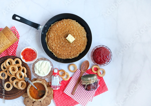 Photography Pancakes on frying pan, red caviar, sour cream, jam, honey,  traditional folk doll on light background