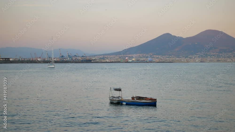 Small boats in the evening in Naples and view on Vesuvius on the horizon in August. Wide shot, handheld.