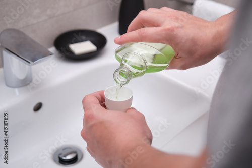 Man pouring green mouthwash from bottle into cap in bathroom. Teeth care concept. photo