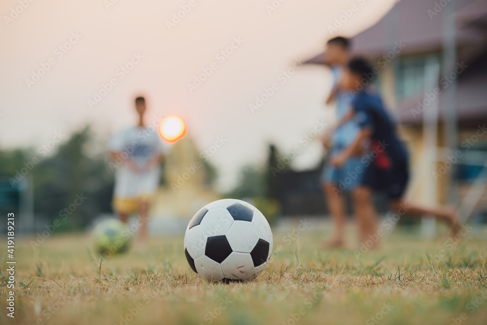 Fototapeta premium Action sport outdoors of kids having fun playing soccer football for exercise in community rural area under the twilight sunset sky. Fresh and vibrant image with anonymous people.