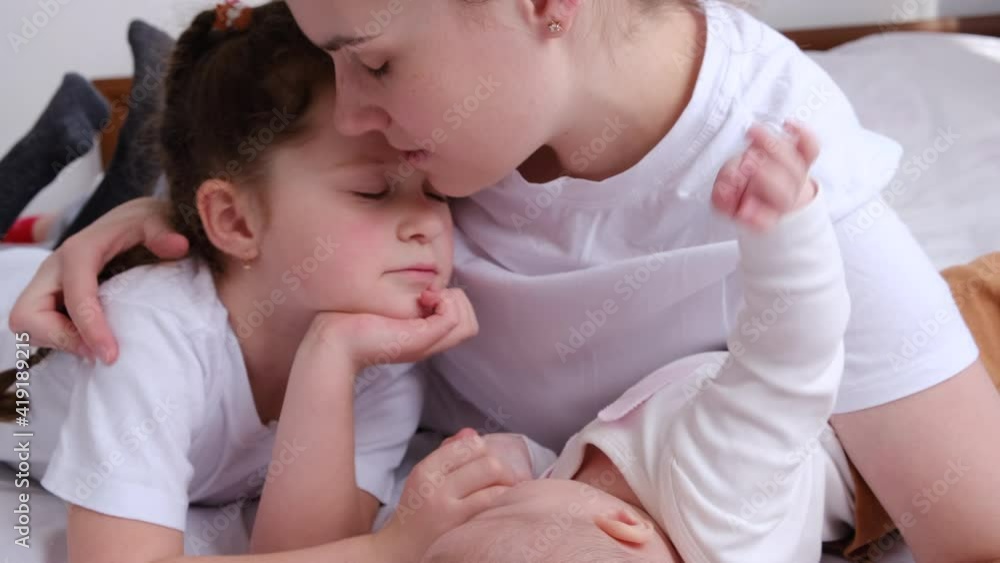 Loving happy young mother lying on bed with two little daughter, kiss cuddle. Smiling caring mom enjoy close tender family weekend moment with small toddler childs. Relish tender moment concept Loving happy young mother lying on bed with two little daughter, kiss cuddle. Smiling caring mom enjoy close tender family weekend moment with small toddler childs. Relish tender moment concept