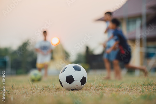 Fototapeta Naklejka Na Ścianę i Meble -  Action sport outdoors of kids having fun playing soccer football for exercise in community rural area under the twilight sunset sky. Fresh and vibrant image with anonymous people.