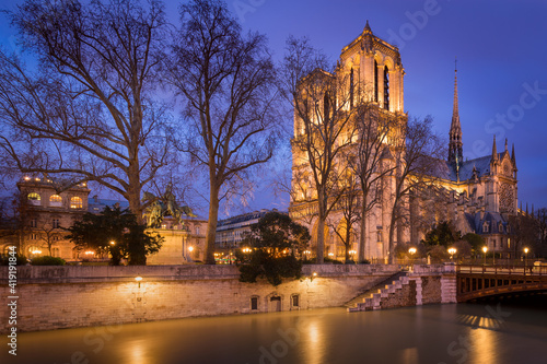 Notre Dame de Paris cathedral illuminated at dusk with the Seine River banks (UNESCO World Heritage Site). Ile de la Cite, Paris, France