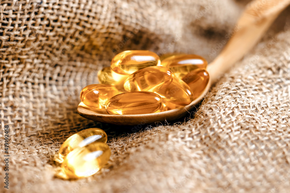 Fish oil capsules in a wooden spoon. Fish oil pills, tablets on the burlap. Vitamin complex omega 3,6,9. Fish oil capsules with omega-3, vitamin D. Close up Fish oil capsules in a wooden spoon. Fish oil pills, tablets on the burlap. Vitamin complex omega 3,6,9. Fish oil capsules with omega-3, vitamin D. Close up