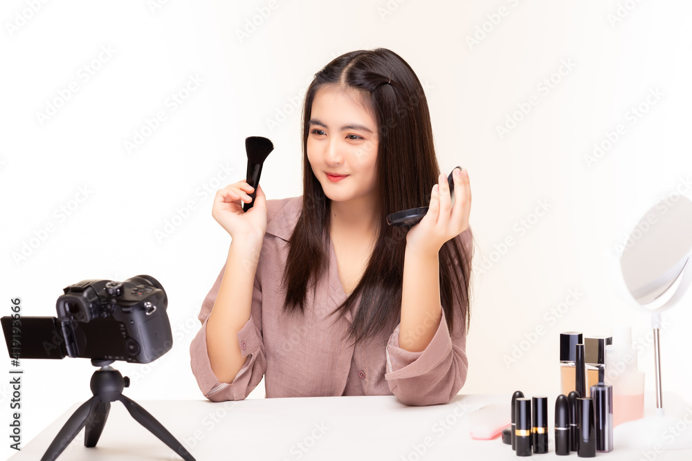 Young woman blogger presenting beauty product and broadcasting live video on social network by using camera Influencer beautician woman show foundation on her beauty face and holding makeup brush Young woman blogger presenting beauty product and broadcasting live video on social network by using camera Influencer beautician woman show foundation on her beauty face and holding makeup brush