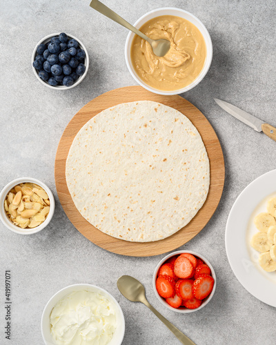 Tortilla cooking process with different fillings of peanut butter, banana, strawberry, blueberry, almond. Food trend. Sweet sandwich for breakfast. Trendy way of wrapping. Top view, copy space