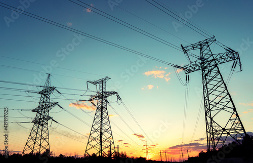 silhouette of high voltage power lines against a colorful sky at sunrise.