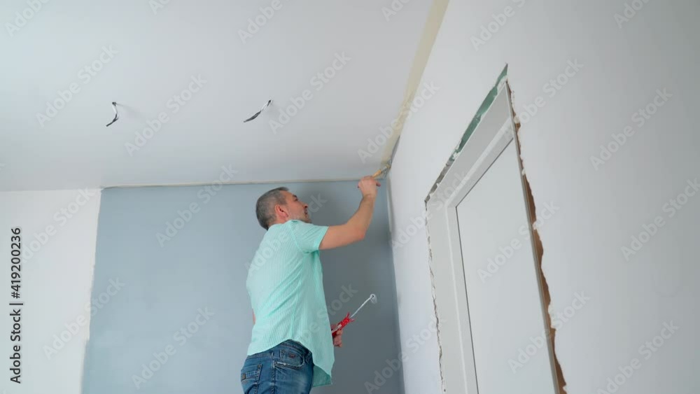 A man in a shirt Paints the walls with a roller gray. Repair of the premises. A man in a shirt Paints the walls with a roller gray. Repair of the premises.