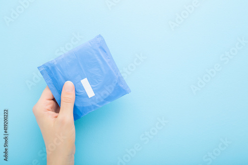 Young adult woman hand holding pack of sanitary towel on light blue table background. Pastel color. Closeup. Protection in night time. Empty place for text. Top down view.