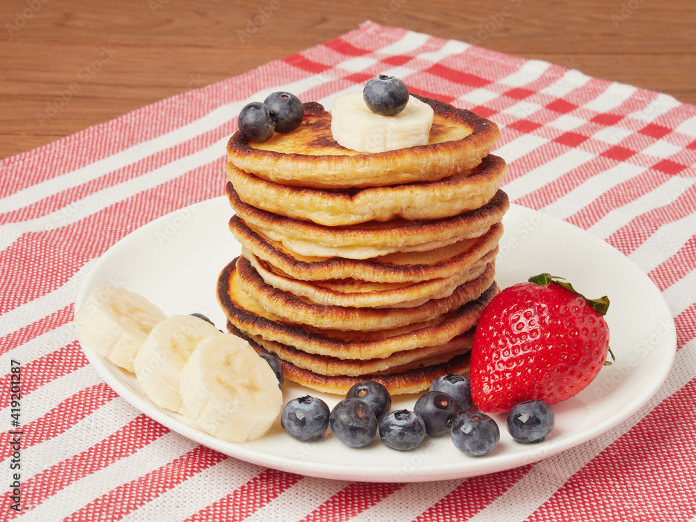 Close-up of delicious pancakes, with fresh blueberries, strawberries and maple syrup on a light background. With space to copy. Sweet maple syrup flows from a stack of pancakes
