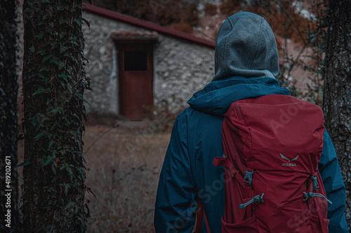 Boy who is traveling between the mountains, is traveling a path and it is dark, with bad weather, mysterious landscape. He is wearing red bag and blue jacket.