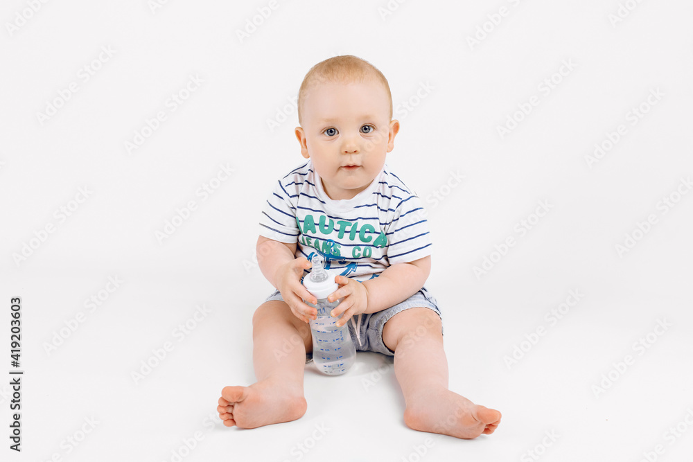 Smiling little child holding bottle with milk while sitting on white background Smiling little child holding bottle with milk while sitting on white background