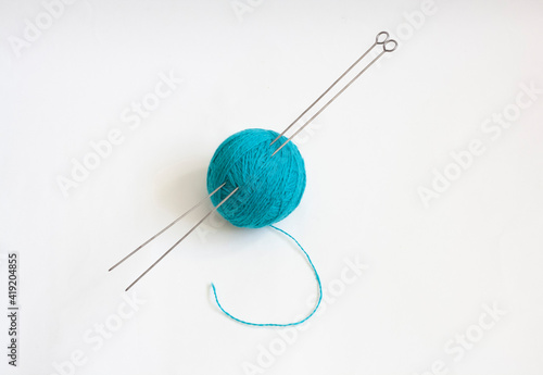 A skein of blue knitting thread and knitting needles on a white background