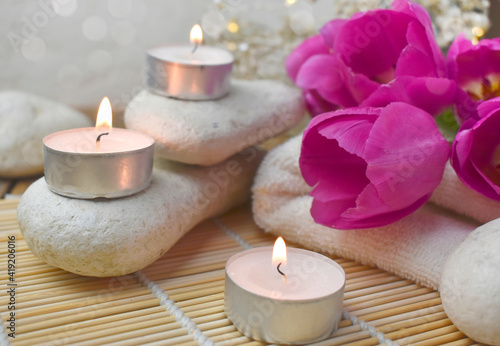 Close spa massage composition with pebbles, tulips, burning candles. Springtime wellness concept. Relaxation. Greeting card for Mothers day or wedding.