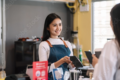 Image of the Asian coffee shop owner smiling beautifully providing phone payment service to customers at the café.