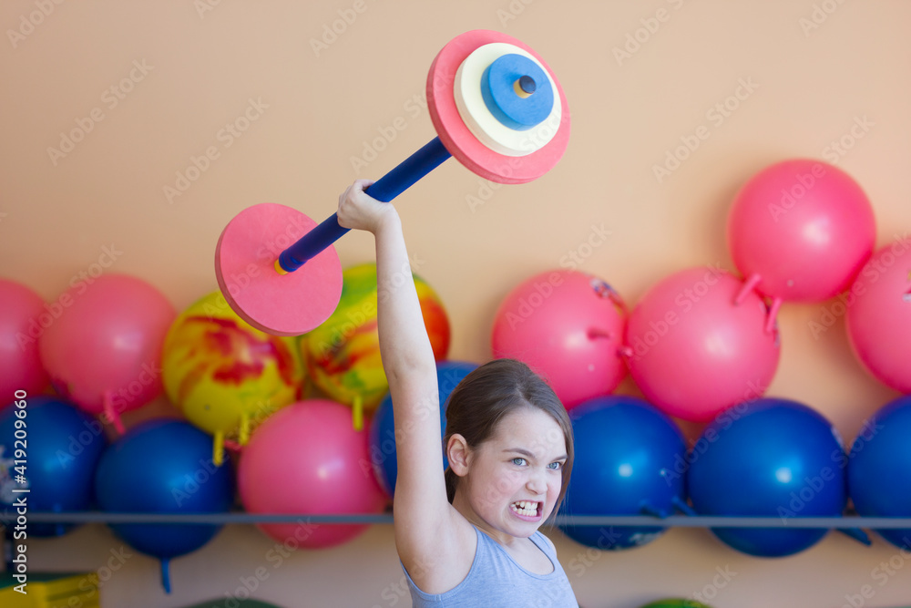 Obraz premium Little girl holding a barbell in the gym