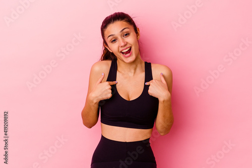 Young sport Indian woman isolated on pink background surprised pointing with finger, smiling broadly. © Asier