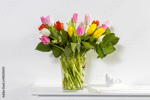 A bouquet of multi-colored tulips in a transparent vase and cup of tea