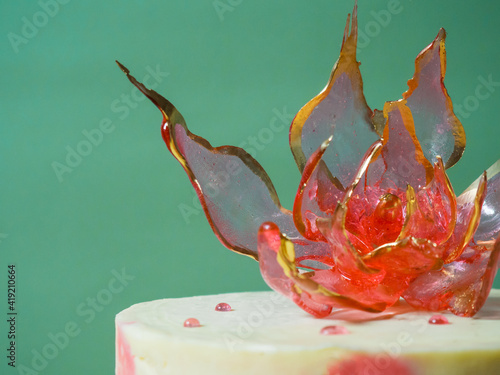 An edible red isomalt flower on top of a cake on a pale green background photo