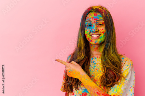 Young Indian woman celebrating holy festival isolated on white background smiling and pointing aside, showing something at blank space.
