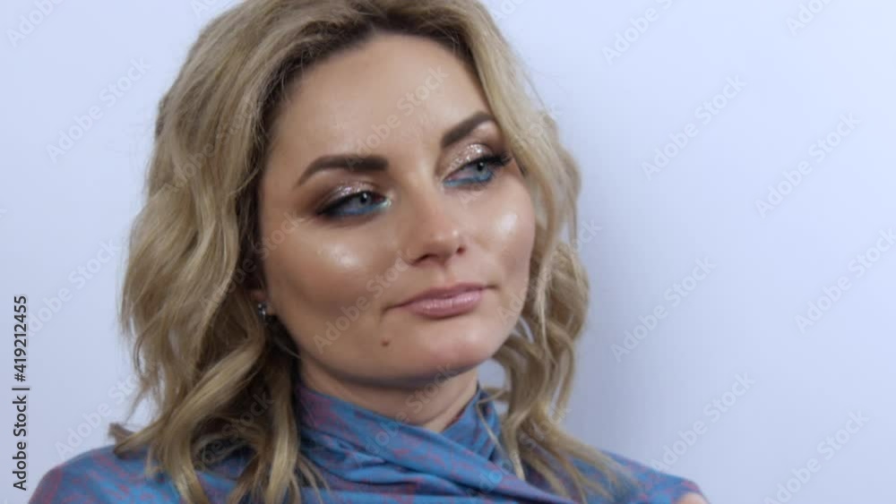 Beautiful young woman with bright evening make-up smoky eyes, freezes and wraps herself in a blue scarf. Girl model thoughtfully looks to the side on a white background. Beautiful young woman with bright evening make-up smoky eyes, freezes and wraps herself in a blue scarf. Girl model thoughtfully looks to the side on a white background.
