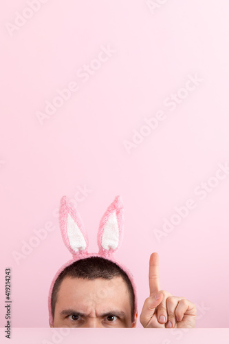 A man on a pink background, with pink rabbit ears on his head. Concept for Easter celebrations, emotions on face. Copy space.