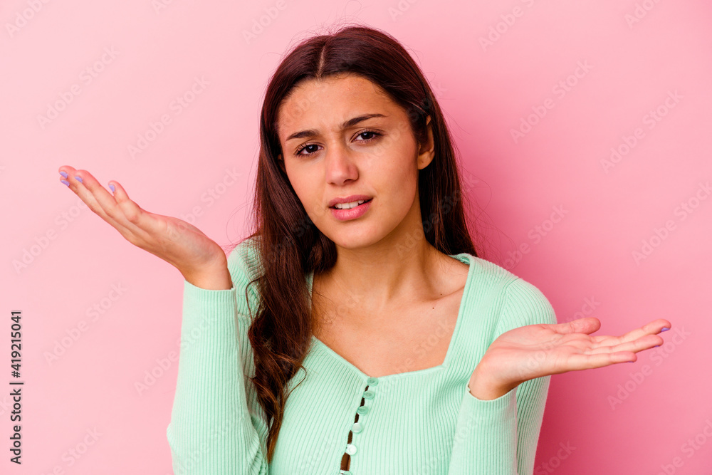 Young Indian woman isolated on pink background confused and doubtful shrugging shoulders to hold a copy space. Young Indian woman isolated on pink background confused and doubtful shrugging shoulders to hold a copy space.