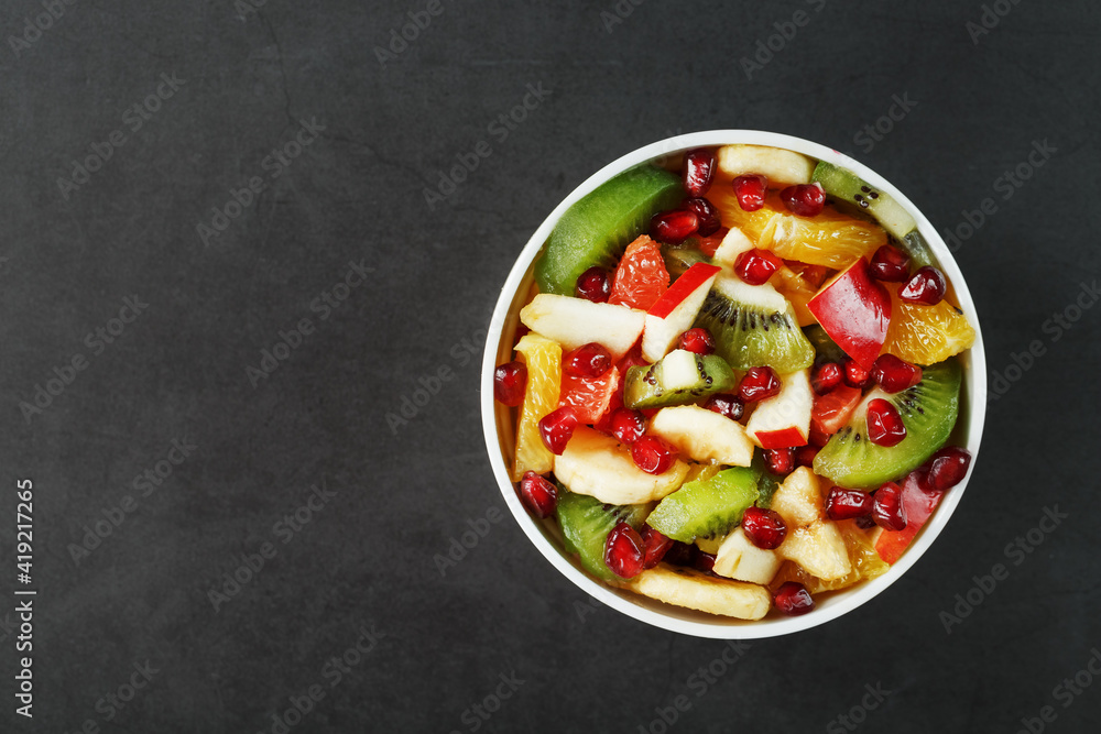 Fruit salad in a white cup on a black background, free space for text. Fruit salad in a white cup on a black background, free space for text.