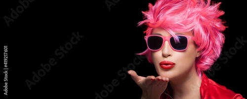 Beautiful model girl with trendy modern sunglasses and stylish pink short hair sending a kiss with pouting red lips