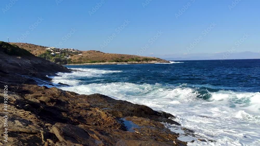 White stormy waves hitting rocks on shore with blue vivid water. Coast near Athens in Greece. Summer nature vacation travel to Aegean Sea White stormy waves hitting rocks on shore with blue vivid water. Coast near Athens in Greece. Summer nature vacation travel to Aegean Sea