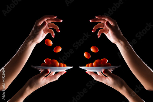 Composition of cherries tomatoes, falling from hands, on a plate with black background and high contrast.Cherries tomatoes on black background.