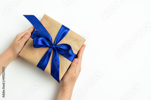 Gift box with a blue ribbon in the hands of a child on a white background. Fathers day, birthday and holiday concept. Top view, flat lay, copy space