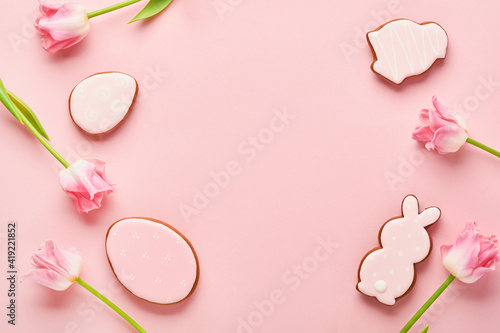 Easter greeting card with easter gingerbread eggs and tulip flowers over pink background. Top view flat lay with copy space