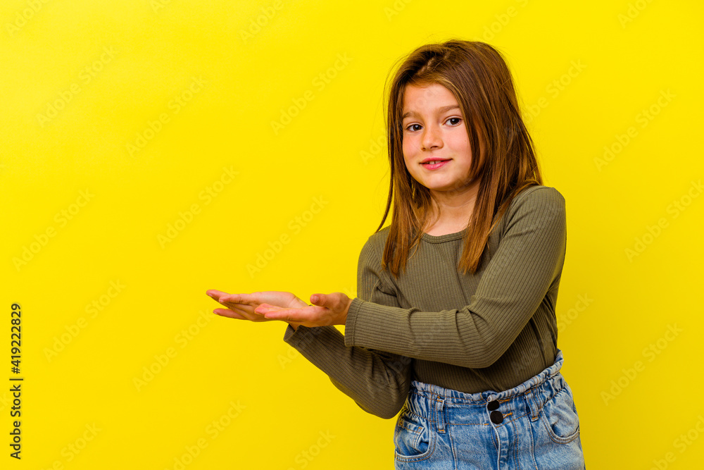 Little caucasian girl isolated on yellow background holding a copy space on a palm. Little caucasian girl isolated on yellow background holding a copy space on a palm.