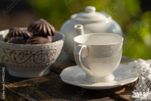 Elegant cup, lace tablecloth, teapot, marshmallow in chocolate, wooden table. Outdoor breakfast, picnic, brunch, spring mood. Soft focus